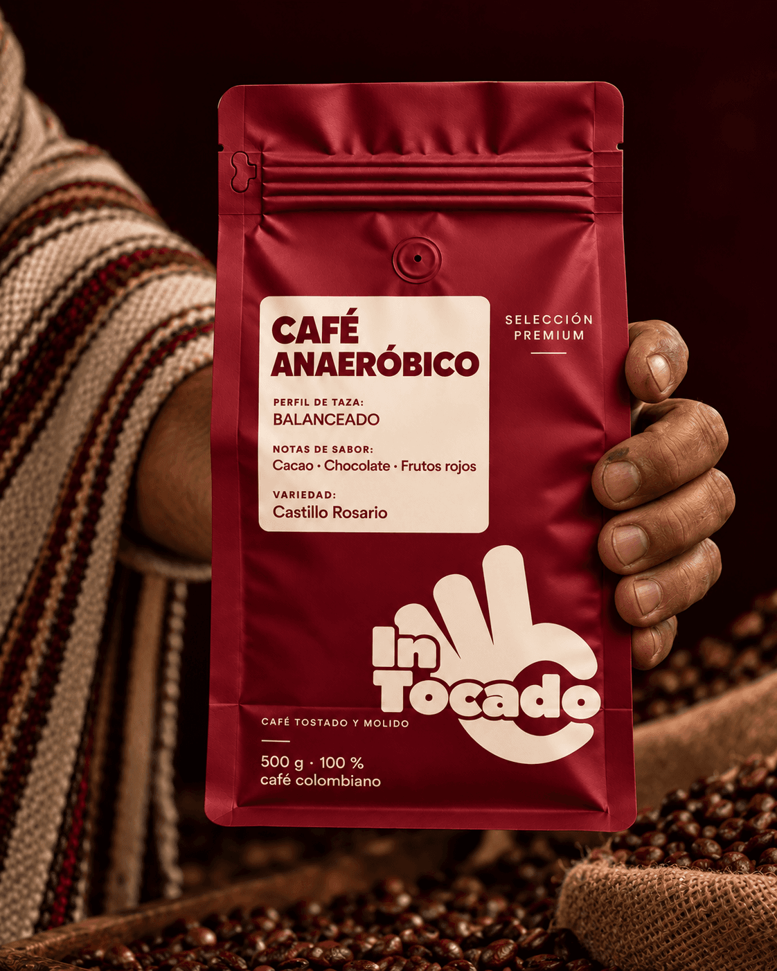 Mano de caficultor sosteniendo una bolsa de café Intocado anaeróbico sobre granos tostados